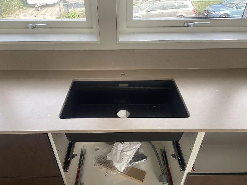 Underlimmad svart kompositdiskho i en bänkskiva av matt Silestone Coral Clay under fönster i ett kök i Kalmar.
