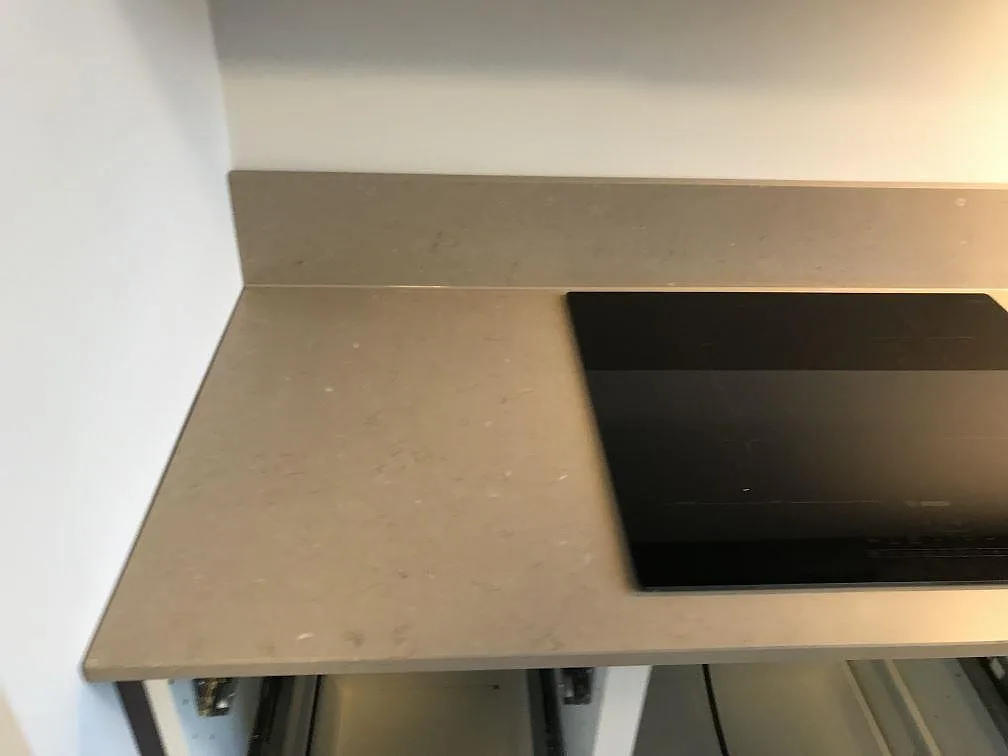 Matt Silestone Coral Clay köksbänkskiva med svart induktionshäll och uppvikt stänkkant mot vägg i ett kök i Kalmar.
