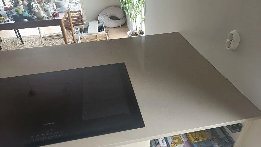 Köksö i Silestone Coral Clay med infälld induktionshäll och polerad yta som speglar ljuset i ett kök i Kareby.