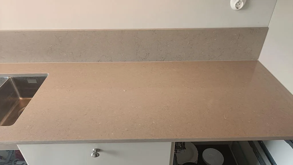 Bänkskiva i Silestone Coral Clay med uppvikt stänkkant och underlimmad diskho i greige kvartskomposit i ett kök i Kareby.