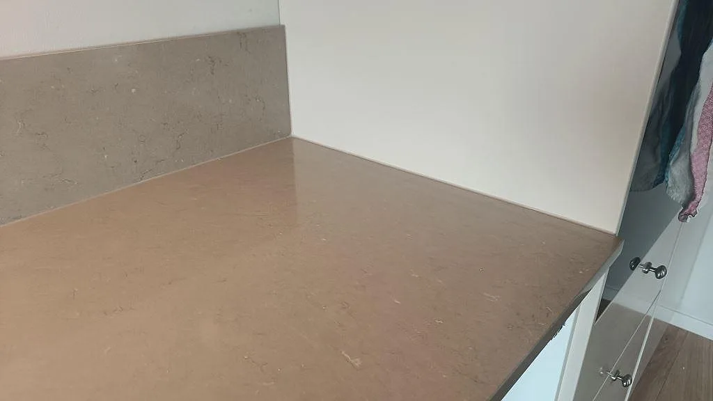Hörnparti av en polerad köksbänkskiva i Silestone Coral Clay med uppvikt stänkkant i ett kök i Kareby.
