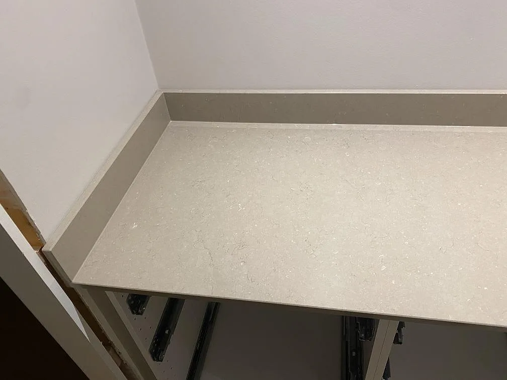 Bänkskiva i polerad Silestone Coral Clay mot vägg med uppvikt stänkkant ovanför öppna stommar i ett kök i Karlskrona.