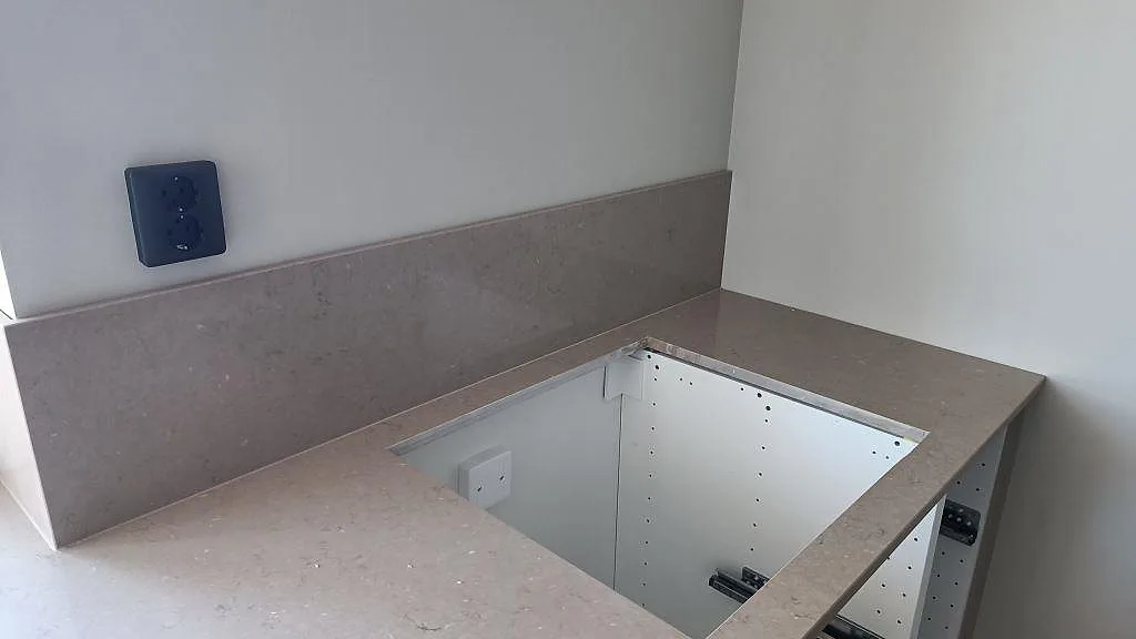 Detalj av gråbeige Silestone Coral Clay kvartskomposit, polerad, med förberett hälluttag och stänkskydd mot väggen i Karlskrona.