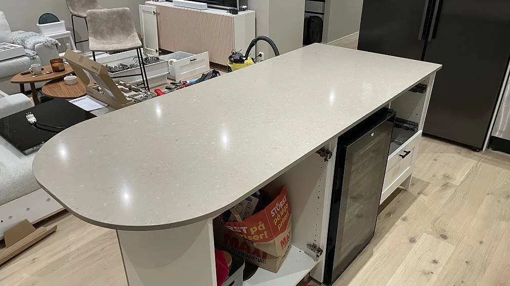 Närbild på köksö i polerad Silestone Coral Clay, kvartskomposit, med vit stomme och rundad ände i Karlskrona.