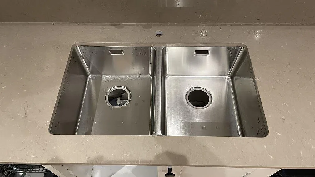 Detalj av rostfri dubbelho i polerad Silestone Coral Clay, kvartskompositbänkskiva med matchande stänkskydd i Karlskrona.