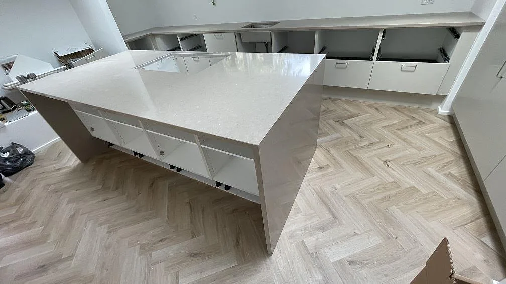 Stor köksö i polerad Silestone Coral Clay med neddragna stengavlar och urtag för häll i ett ljust kök i København.