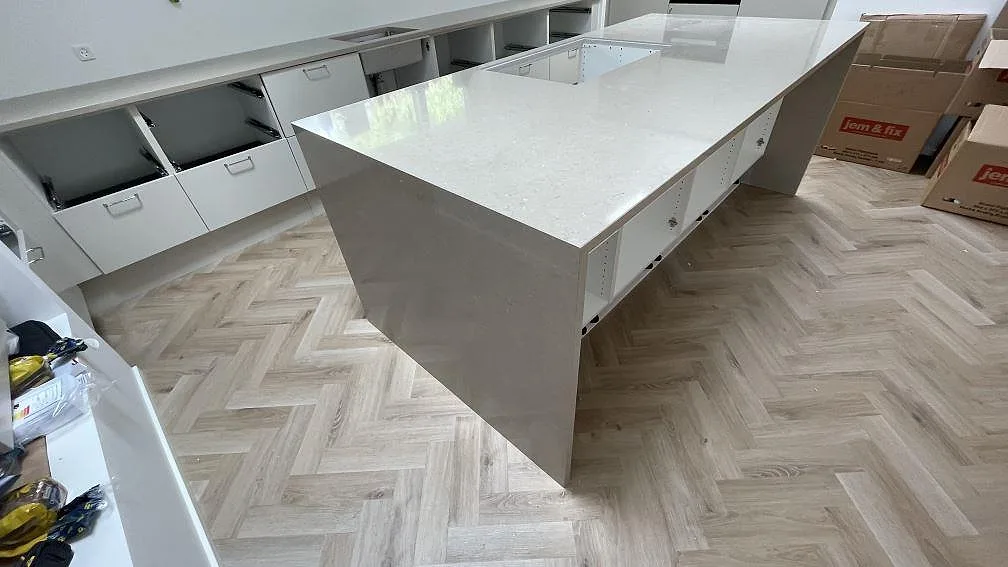 Köksö i polerad Silestone Coral Clay sedd från sidan med ljus gråbeige yta, öppna köksstommar och fiskbensmönstrat golv i København.