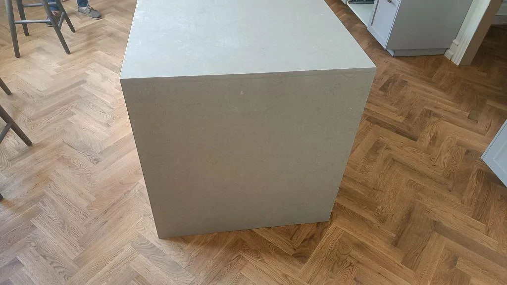Köksö i Silestone Coral Clay med stenklädd gavel mot fiskbensparkett i ett kök i København Ø.