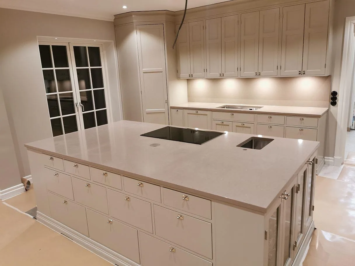 Köksbänkskiva i Silestone Coral Clay, polerad greige kvartskomposit, på en stor köksö med induktionshäll i ett ljust kök i Kristianstad.