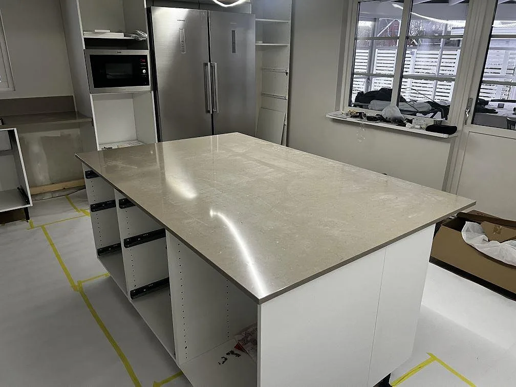 Stor köksö med polerad bänkskiva i Silestone Coral Clay, greige kvartskomposit, under montering i ett kök i Kristianstad.