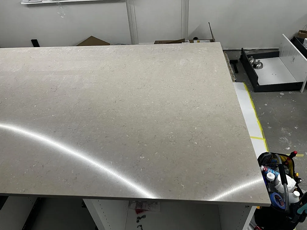 Närbild ovanifrån på den polerade greige Silestone Coral Clay-ytan på köksön under montering i Kristianstad.