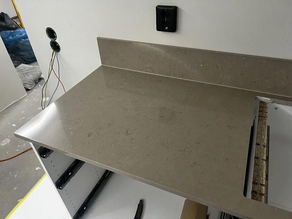 Väggbänk i Silestone Coral Clay med uppvikt stänkskydd, eluttag och öppna skåpstommar under montering i Kristianstad.