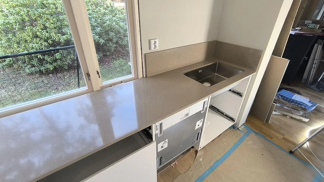 Polerad bänkskiva i Silestone Coral Clay komposit med diskho och stänkskydd längs fönsterväggen i Kungsängen.