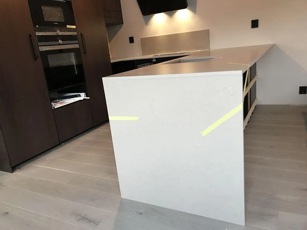 Köksbänkskiva i matt Silestone Coral Clay, varm gråbeige kvartskomposit, med köksö och stänkskydd i ett kök i Kungsbacka.