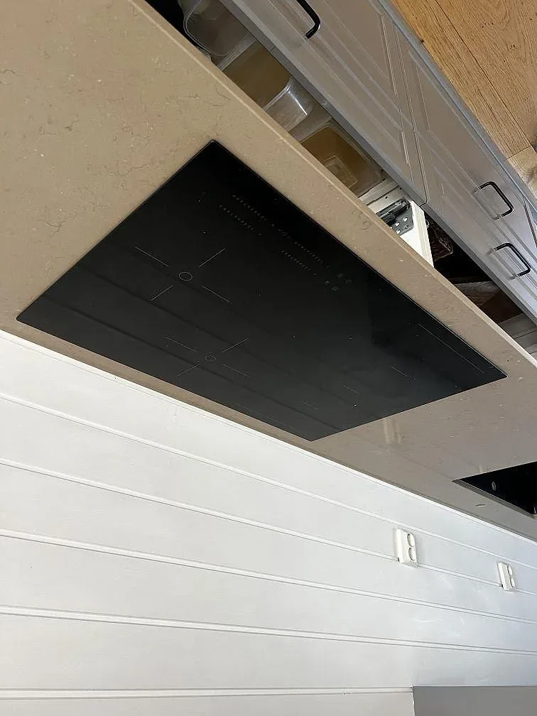 Infälld svart induktionshäll i den polerade Silestone Coral Clay-bänkskivan mot vit pärlspontvägg i ett kök i Kungsbacka.
