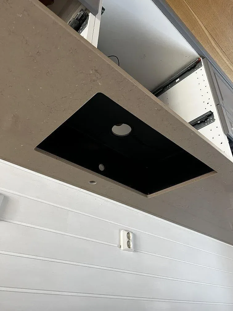 Närbild på den underlimmade mörka diskhon i den polerade Silestone Coral Clay-bänkskivan med blandarhål i ett kök i Kungsbacka.