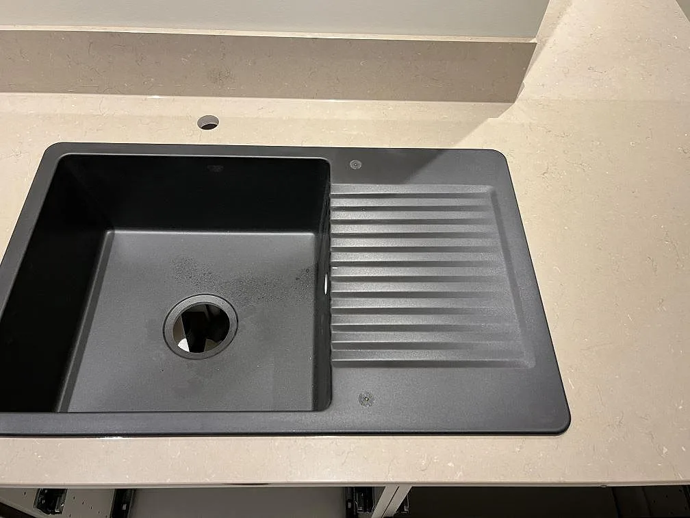 Svart kompositdiskho övermonterad på en polerad köksbänkskiva i Silestone Coral Clay i ett kök i Kungshamn.