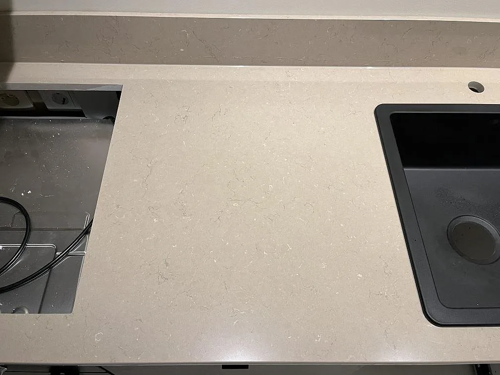 Köksbänk i Silestone Coral Clay i taupe-beige kvartskomposit med svart kompositdiskho och hällurtag sida vid sida i ett kök i Kungshamn.