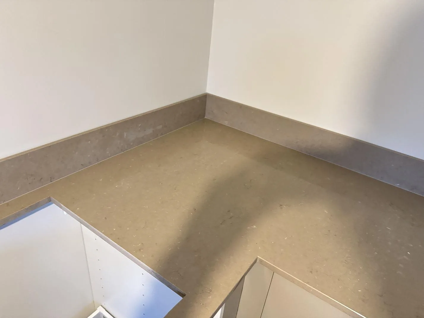 Hörnsektion med polerad Silestone Coral Clay som köksbänkskiva och låg stänkkant längs två väggar i Länghem.