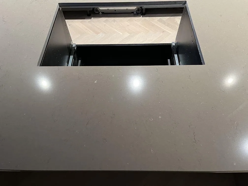 Köksö i greige Silestone Coral Clay med hällurtag, polerad yta som speglar takspotlights, i ett kök i Landskrona.