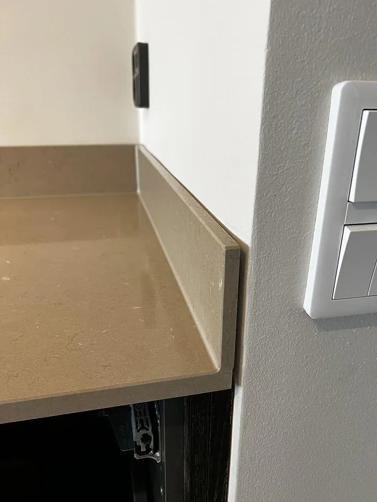 Detalj av kant och låg stänkkant i polerad Silestone Coral Clay vid vägg i Landskrona.