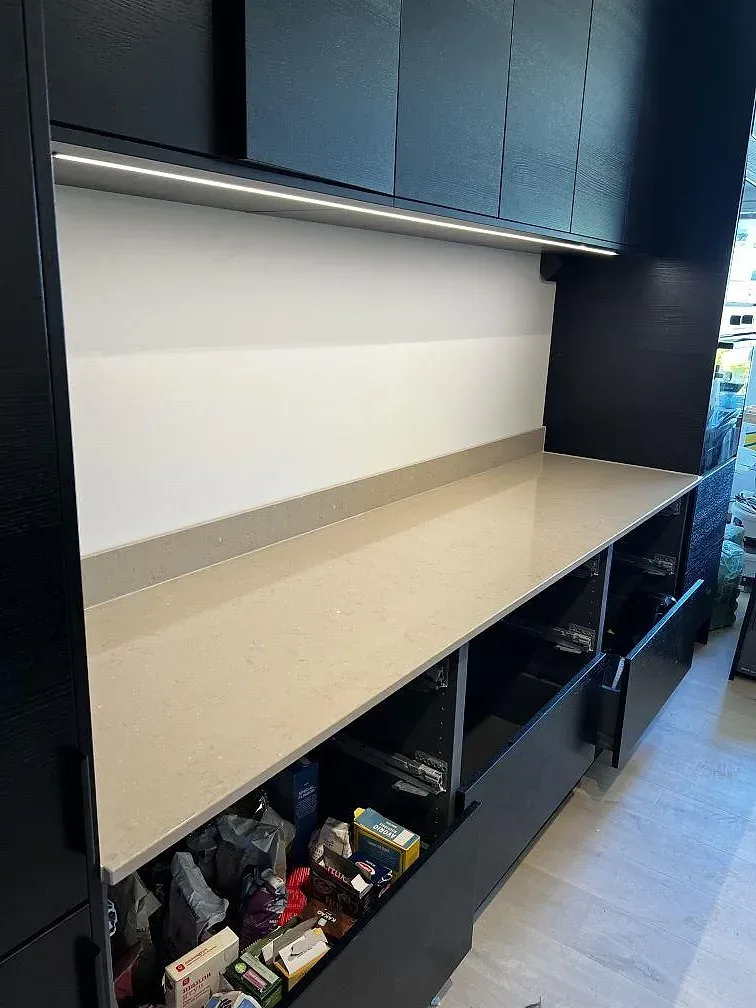 Lång köksbänk i varm gråbeige Silestone Coral Clay, polerad, med låg stänkkant och svart köksinredning i Landskrona.