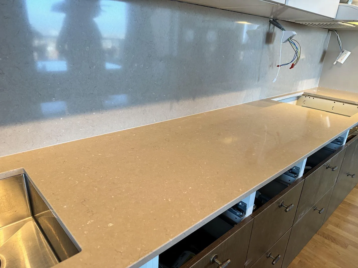 Sammanhängande bänkskiva i polerad Silestone Coral Clay med gråbeige yta, stänkskydd och hällöppning i Landskrona.