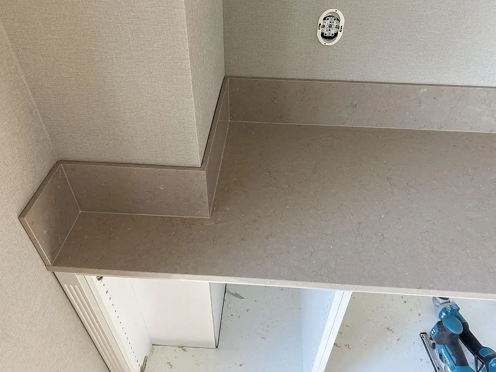 Detalj av polerad Silestone Coral Clay bänkskiva med hörnpassat stänkskydd och beigegrå ådring i Landskrona.