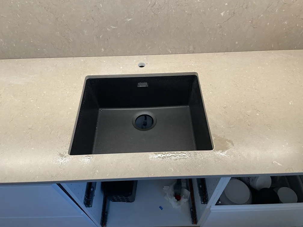 Närbild på svart diskho i matt Silestone Coral Clay köksbänkskiva med beige komposit och stänkskydd i ett kök i Landskrona.