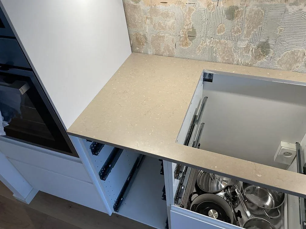 Vänster arbetsyta i matt Silestone Coral Clay med hällöppning, beige komposit och vägg bakom under montering i Landskrona.
