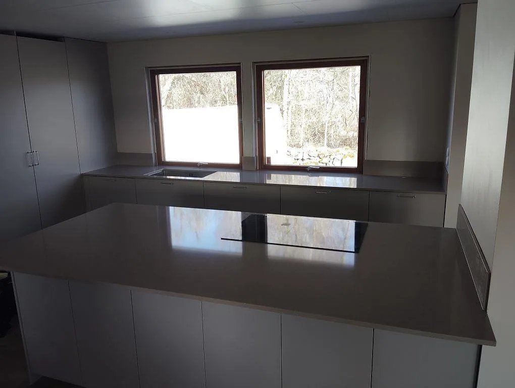Köksbänkskiva i greige Silestone Coral Clay, polerad kvartskomposit, med häll på halvö och diskhozon under fönster i Lillkyrka.