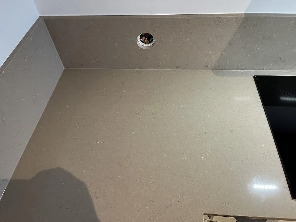 Hörn av Silestone Coral Clay köksbänkskiva med uppvikt stänkkant och urtaget eluttag i Limhamn.