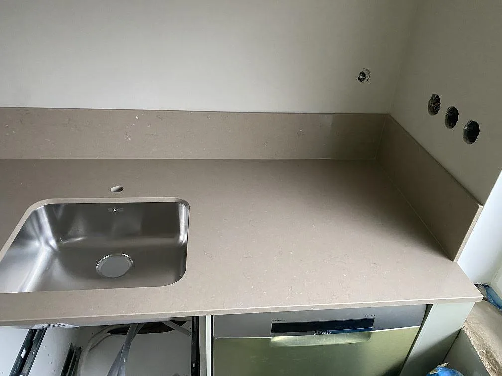 Köksbänkskiva i Silestone Coral Clay, polerad greige kvartskomposit, med underlimmad rostfri diskho och uppvikt stänkkant i ett kök i Limhamn.
