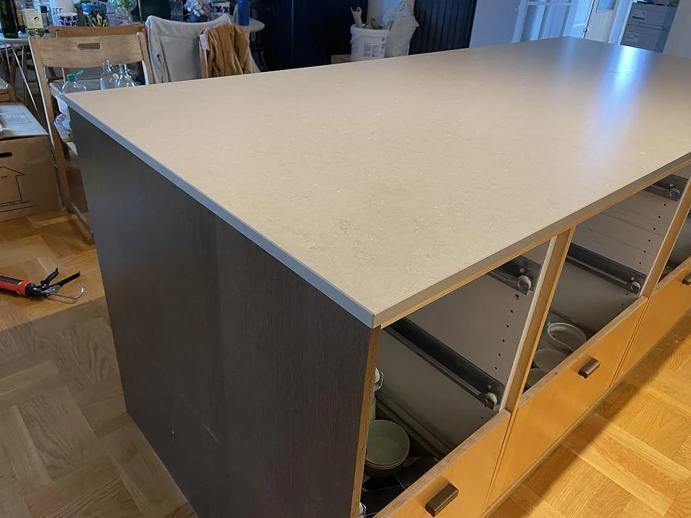 Närbild på köksö i Silestone Coral Clay, matt Mocka-yta, med mörk sidopanel och öppna trästommar under montering i Limhamn.