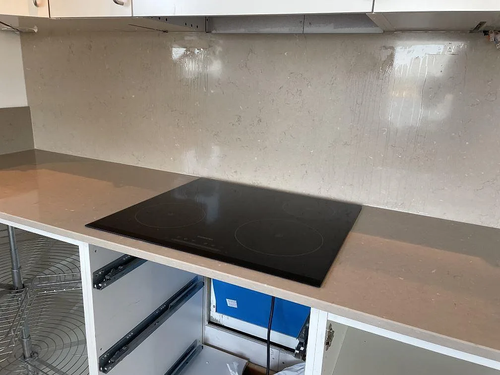 Svart induktionshäll infälld i polerad Silestone Coral Clay med stänkskydd bakom arbetsytan i ett kök i Limhamn.