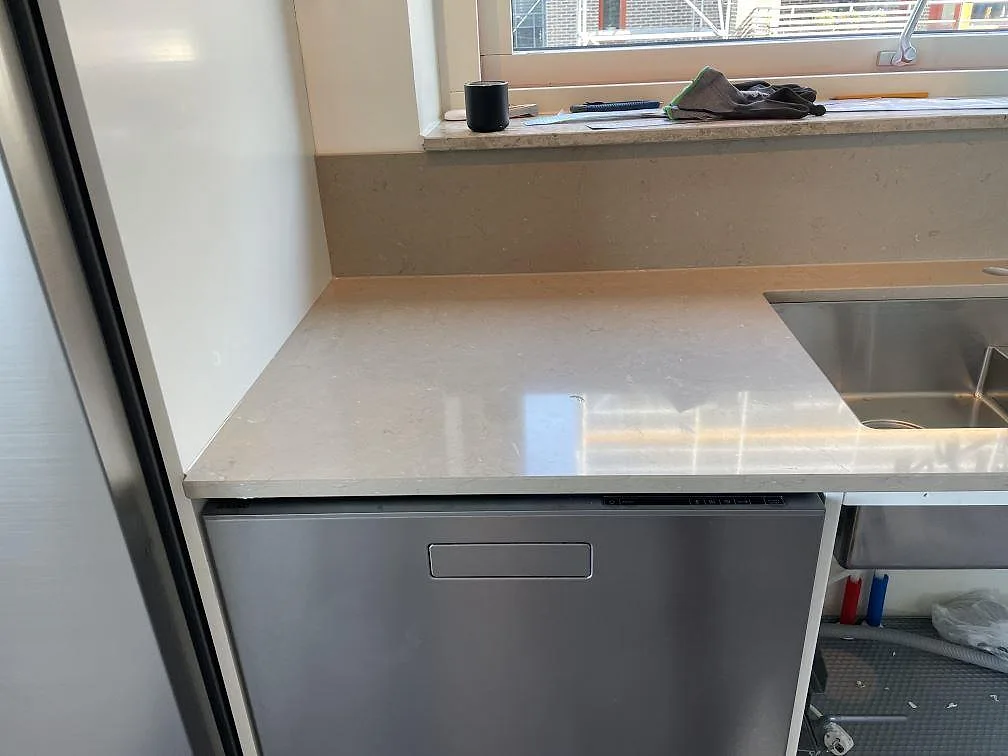 Polerad Silestone Coral Clay ovanför diskmaskin och rostfri diskho, med matchande stänkskydd och fönsterdetalj i Limhamn.