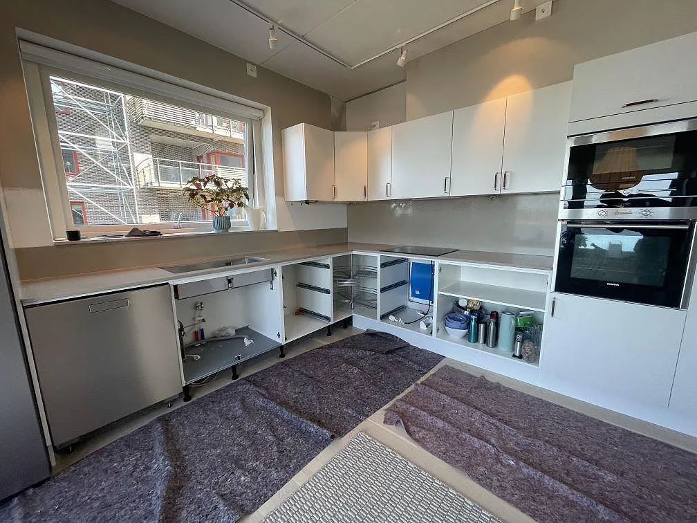 L-format kök i Limhamn med polerad Silestone Coral Clay som köksbänkskiva, stänkskydd, svart induktionshäll och rostfri diskho under montering.