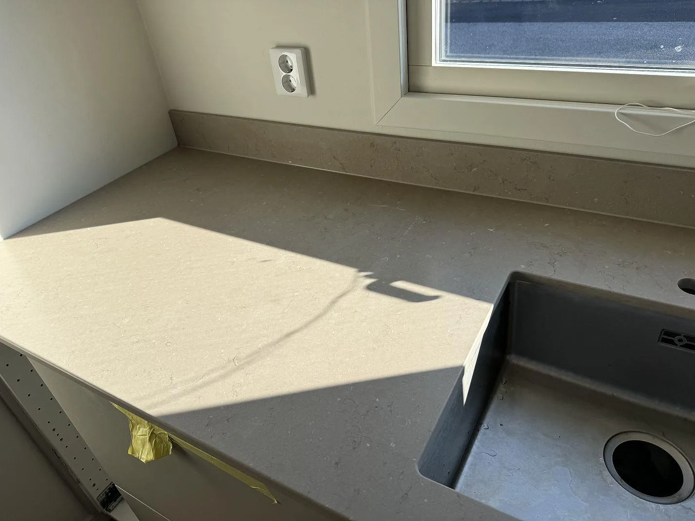 Bänkskiva i Silestone Coral Clay, matt Mocka, längs fönstervägg med låg stänkkant och synlig diskho i Limhamn.