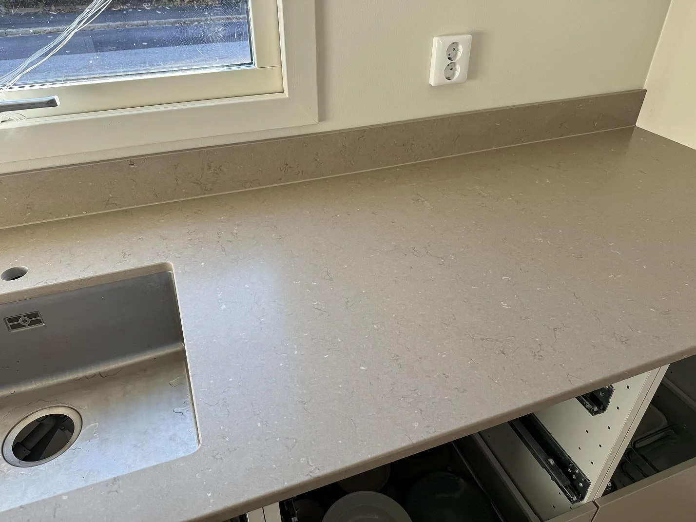 Köksbänkskiva i Silestone Coral Clay, matt Mocka, vid fönster med låg stänkkant och diskhozon i ett kök i Limhamn.