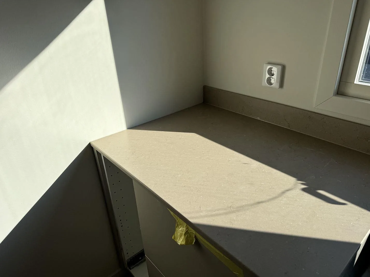 Hörn av köksbänkskiva i Silestone Coral Clay, matt Mocka, med låg stänkkant under fönster i Limhamn.