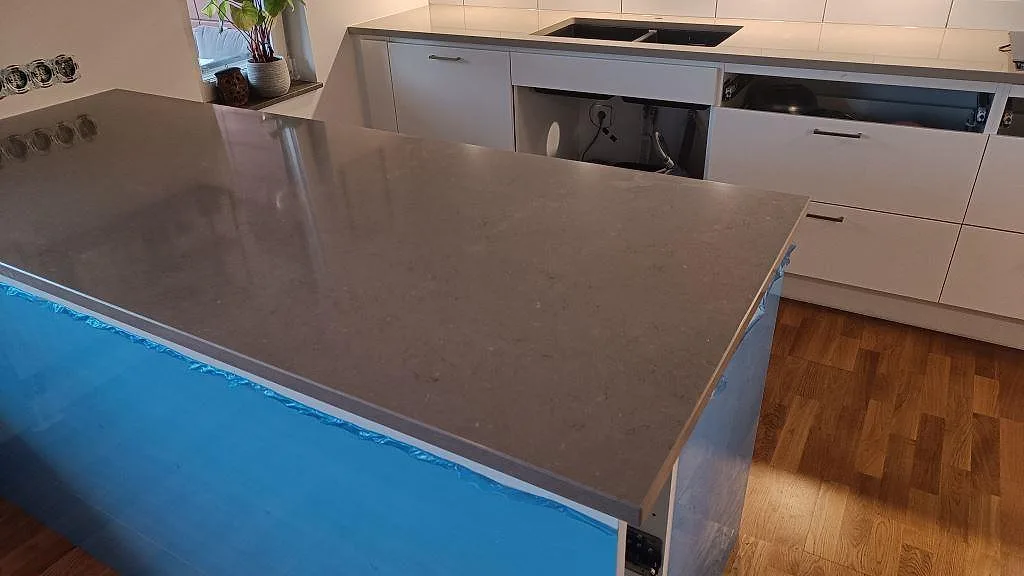 Närbild på köksö med bänkskiva i polerad Silestone Coral Clay, kvartskomposit, framför diskho och skåp i ett kök i Limhamn.