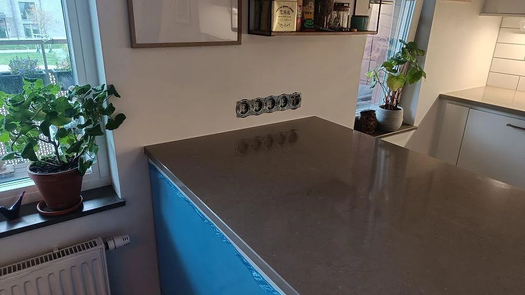 Polerad Silestone Coral Clay som köksö i kvartskomposit med varm gråbeige yta, fönster och vägguttag i ett kök i Limhamn.