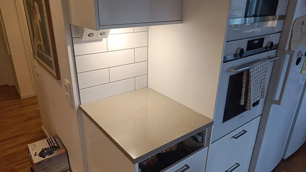 Kort bänkskiva i polerad Silestone Coral Clay, kvartskomposit, vid ugn och vit kakelvägg i köket i Limhamn.