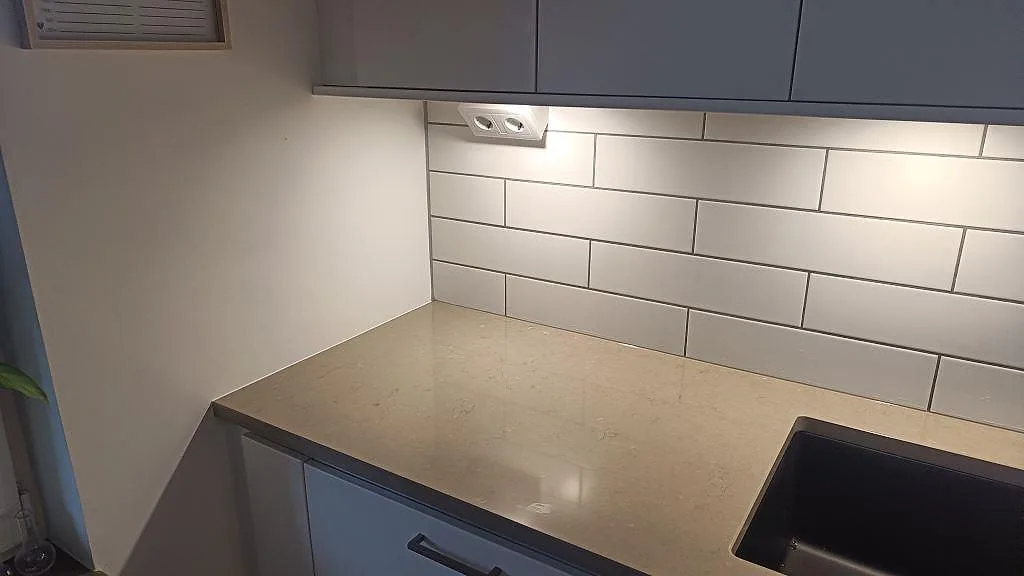 Bänkskiva i polerad Silestone Coral Clay, kvartskomposit, med svart diskho och vitt kakel i köket i Limhamn.