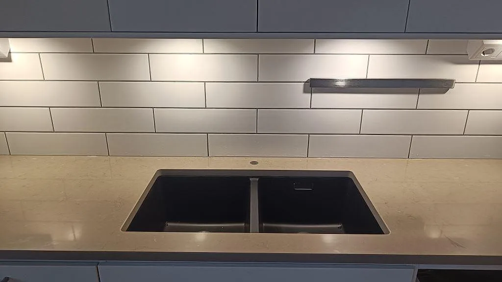 Diskhozonen med svart dubbelho i polerad Silestone Coral Clay, kvartskomposit, vid väggbelysning i ett kök i Limhamn.