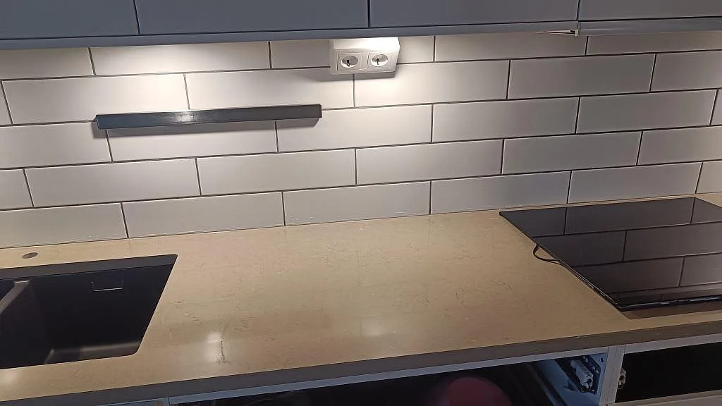 Bänkskiva i polerad Silestone Coral Clay, kvartskomposit, mellan svart diskho och häll vid kakelvägg i ett kök i Limhamn.
