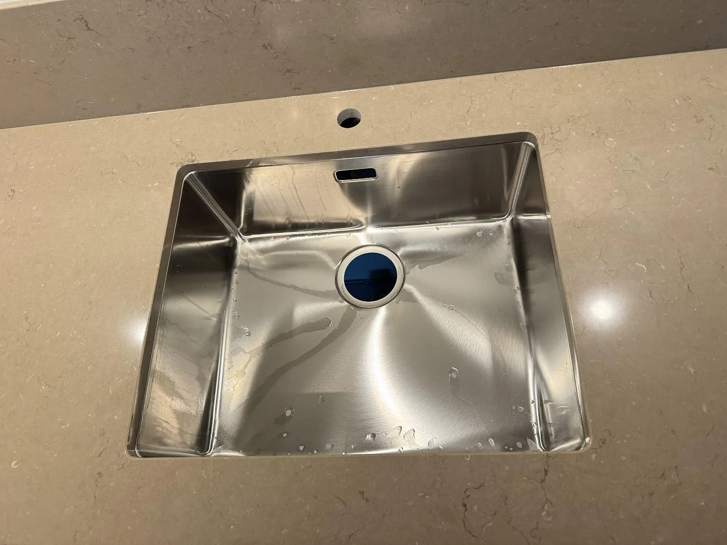 Detalj av rostfri diskho i polerad Silestone Coral Clay, beige kompositbänkskiva i Limhamn.
