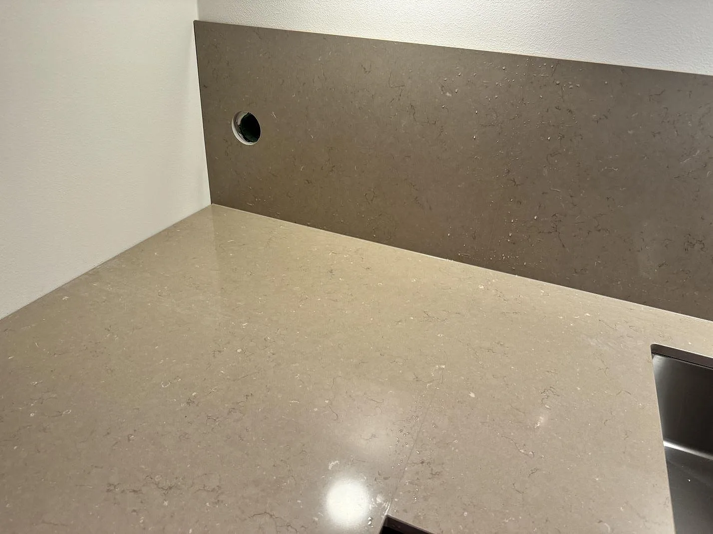 Polerad bänkskiva och mörkare stänkskydd i Silestone Coral Clay med synlig diskhozon i ett kök i Löddeköpinge.