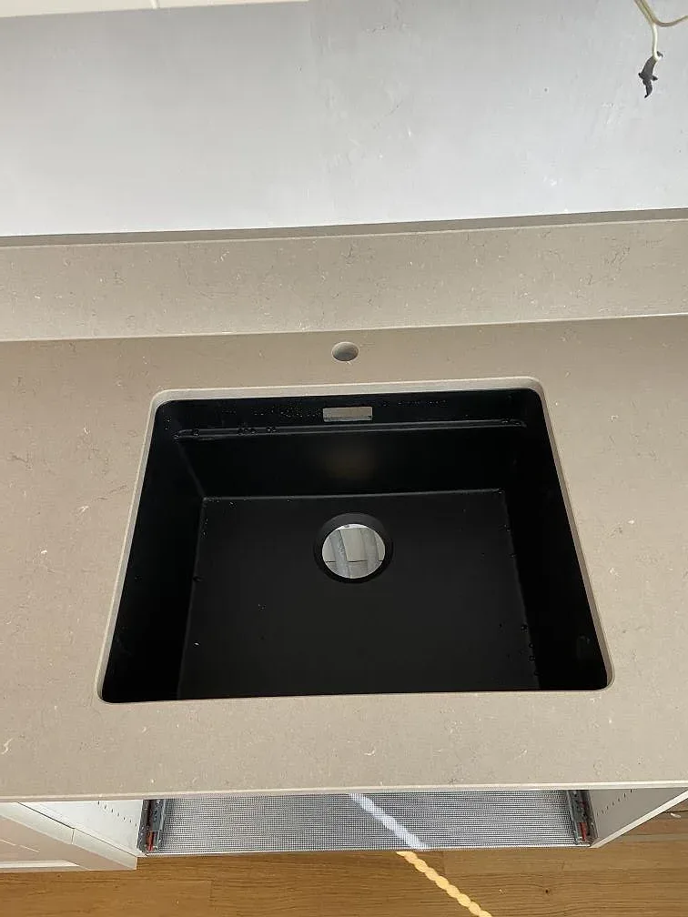 Underlimmad svart kompositdiskho infälld i polerad Silestone Coral Clay bänkskiva med separat blandarhål i ett kök i Lomma.