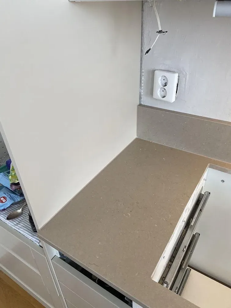 Polerad Silestone Coral Clay bänkskiva med uppdragen stenkant mot väggen och eluttag i ett kök under montering i Lomma.